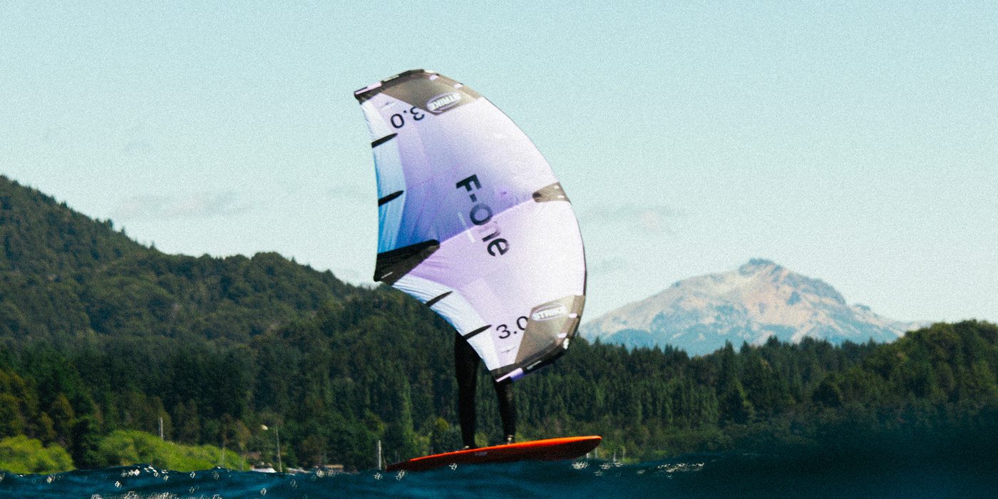 Wingfoiler fliegt auf dem Foil vor Bergkulisse
